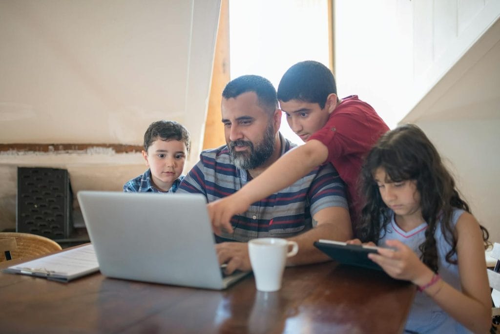 Father and children bonding over digital devices, fostering learning and togetherness.
