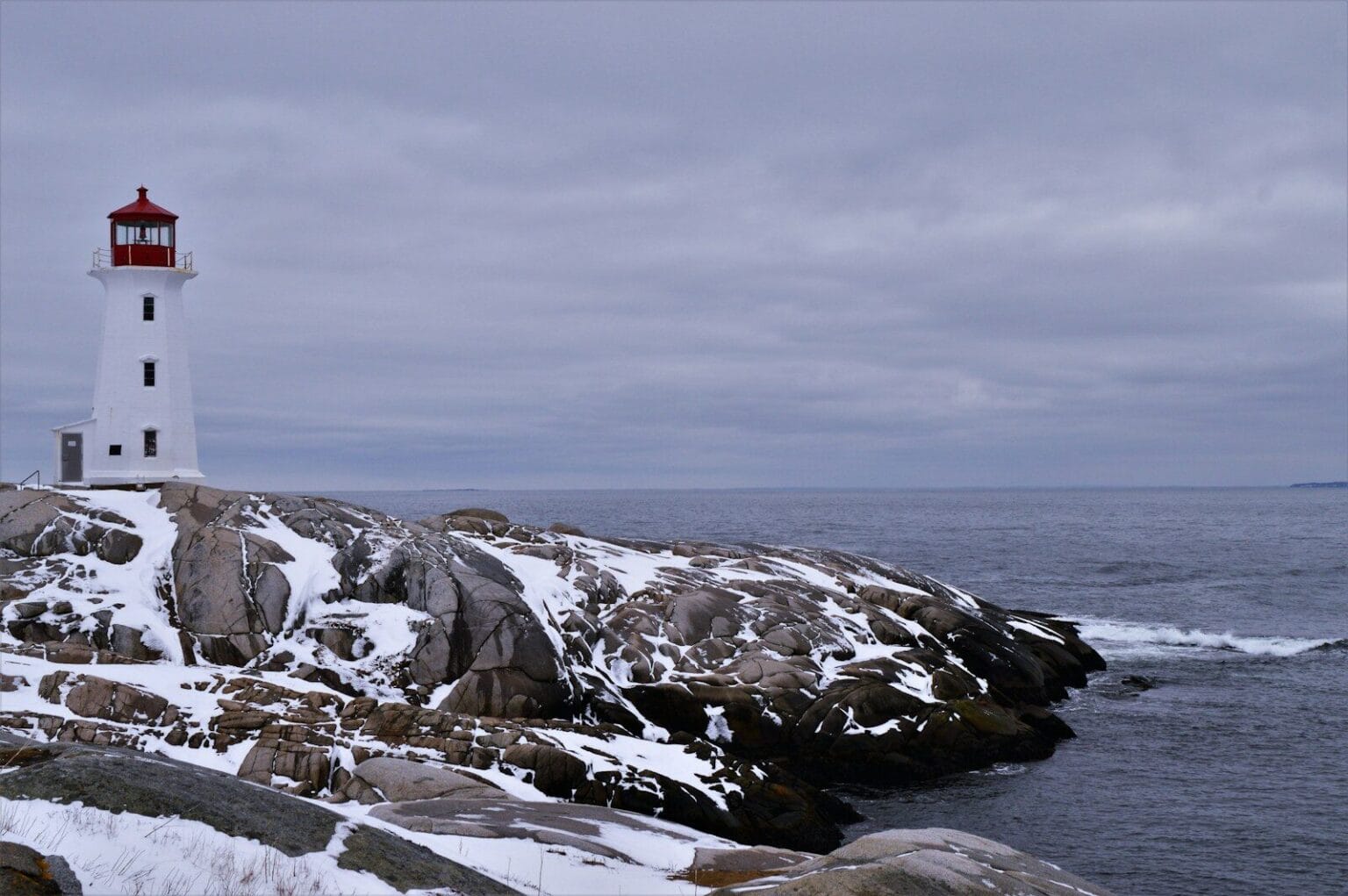 a white and red light house sitting on top of a snow covered rock